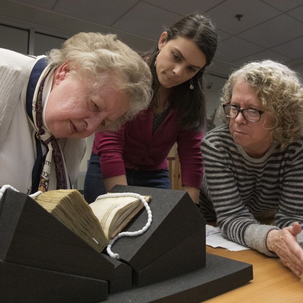 A photograph of 3 scholars looking at the same book