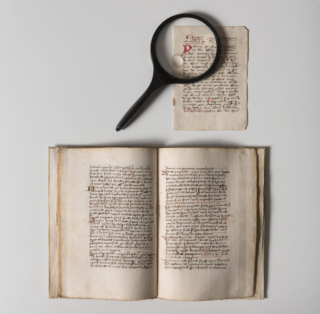 A magnifying glass laid on a manuscript to amplify a red hand scrolled letter "R"