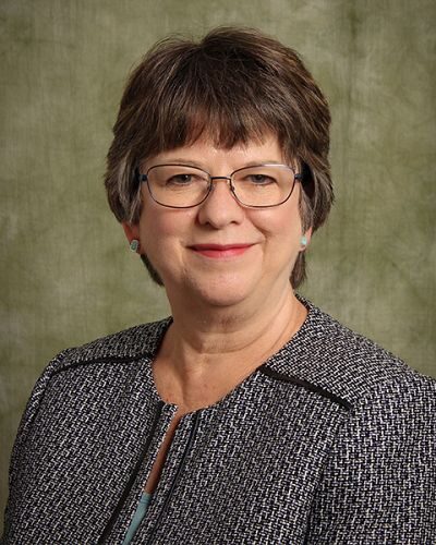 Portrait of a white woman with brown hair wearing wire frame glasses on a green background