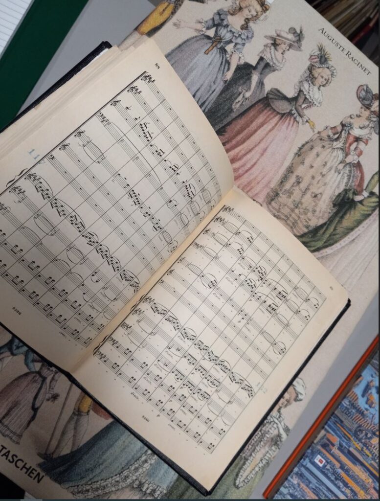 A musical score rests on a background that features women in Victorian dresses