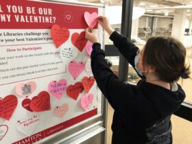 student hangs up heart with a valentine pun written on it during a Valentine's Day outreach event in Bartle Library
