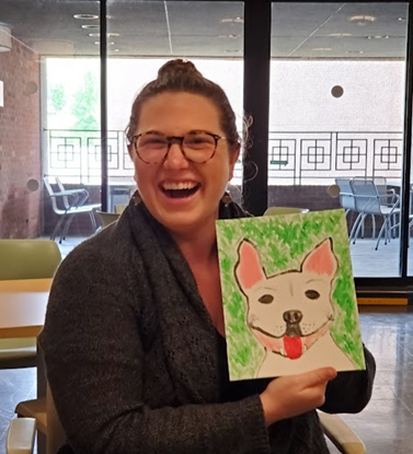 Sr. Associate Head of Reader Services for Patron Experience Anna Norris poses with a painting of a dog she made.