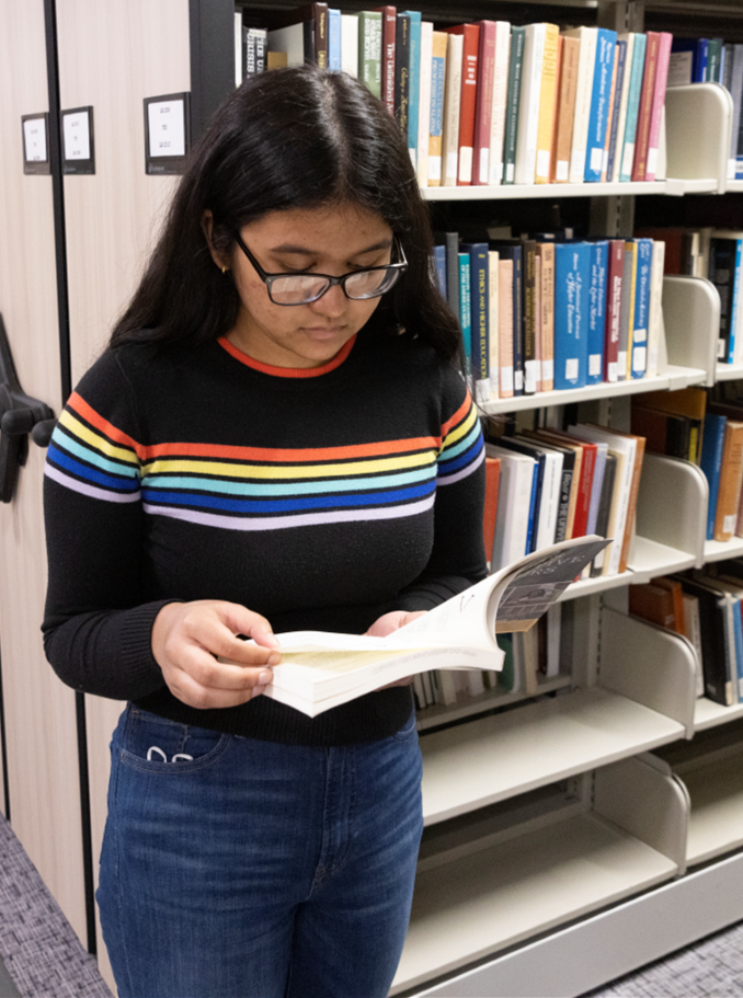 Student leans against the space saving shelving reading a book.