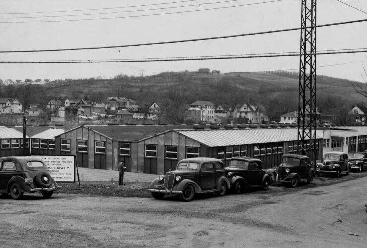 Prefabricated buildings at the first site of Triple Cities College with cars parked in front in 1946