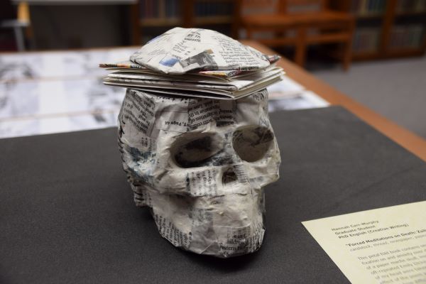 Photograph of a paper mache skull with a petal fold book at the top.