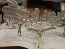 Close up photograph of a book sculpture of a scene of trees, a bridge and a person made from printed pages springing from an open book.
