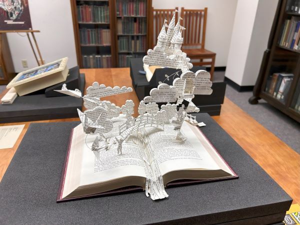 Photograph of book sculpture of a fantasy scene with a castle and clouds made from book pages springing from an open book.