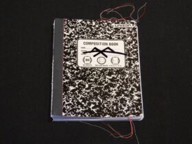 Cover of Alexander Schambach's "Composition, Vol. 1," showing a black and white mottled composition book on a black background, with multi-colored threads at the edges of the book.