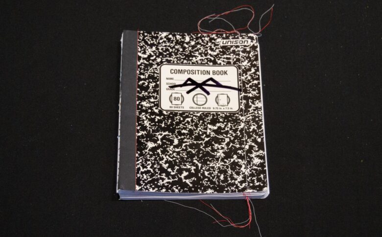 Cover of Alexander Schambach's "Composition, Vol. 1," showing a black and white mottled composition book on a black background, with multi-colored threads at the edges of the book.