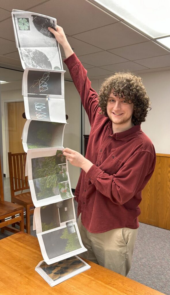 Alexander Schambach holding open his accordion book "Composition, Vol. 1".