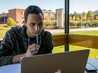 A student sitting beside a large window looks at a computer screen