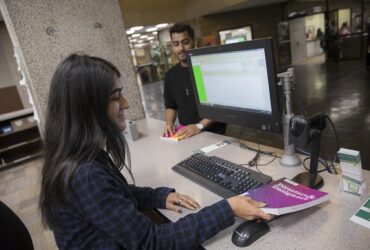 Student library worker checking out book to another student at circulation desk