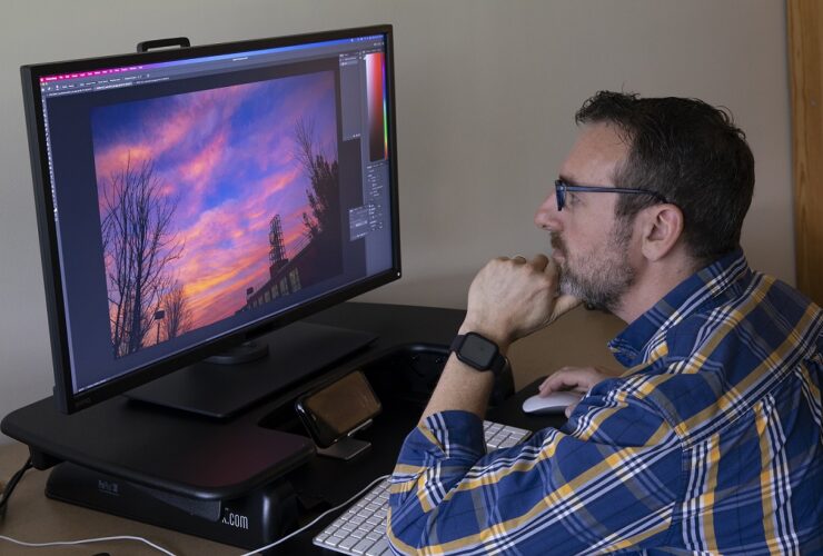 Man sitting at desk looking at image of sunset on a computer