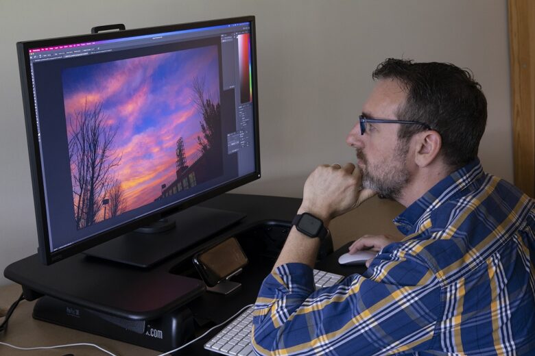 Man sitting at desk looking at image of sunset on a computer