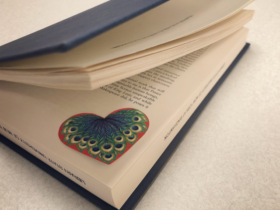 Slightly open book revealing a red heart and peacock feather in the corner.