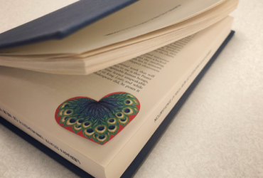 Slightly open book revealing a red heart and peacock feather in the corner.