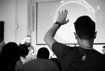 Man wearing black shirt raising his hand in a classroom