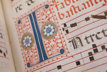 15th century blue and red hand drawn lettering on a white page with black music notes