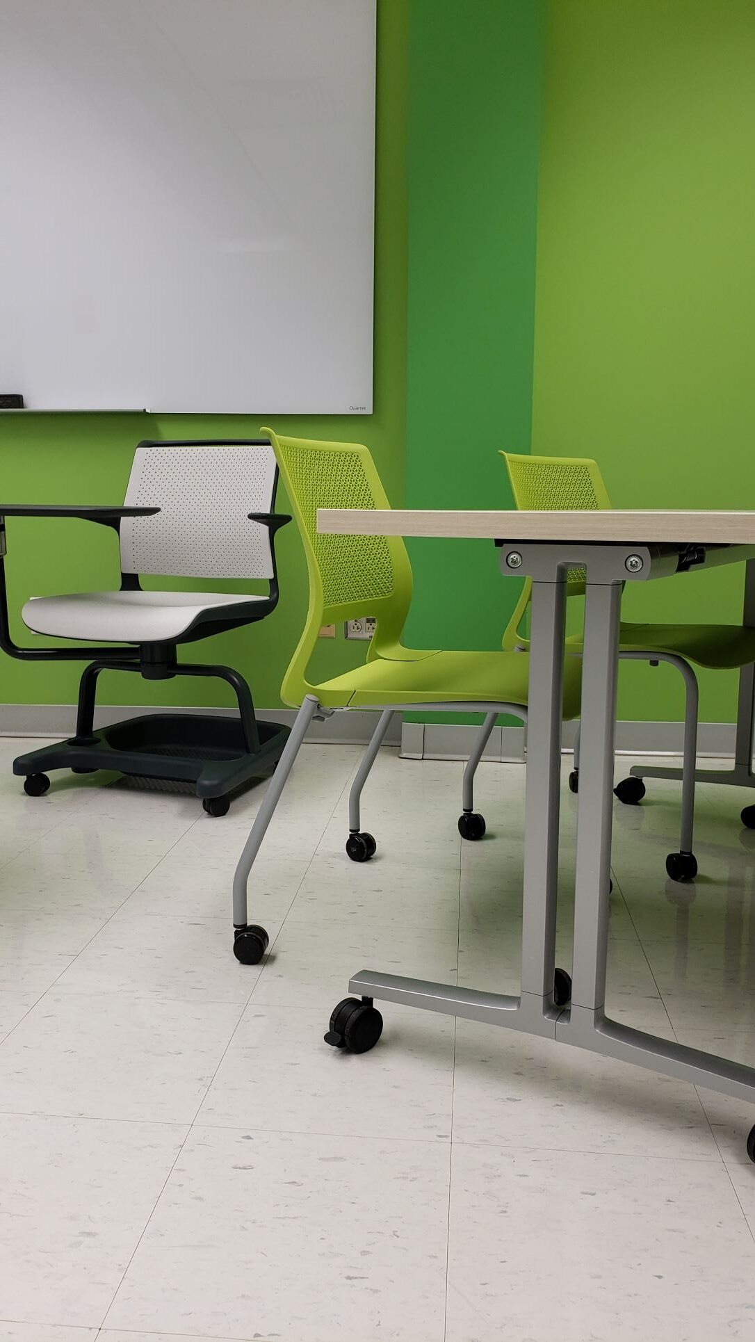 Green chairs with rolling wheels and a grey chair with an attached table in front of a green wall