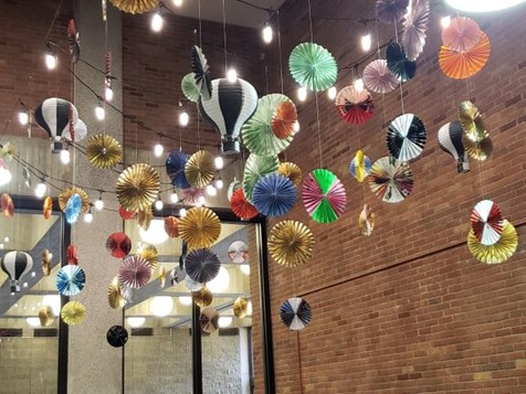 image of colorful paper fans and paper hot air balloons suspended from the ceiling in the Exhibit space