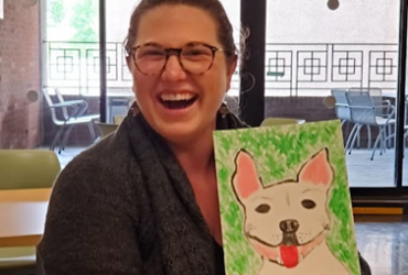 Sr. Associate Head of Reader Services for Patron Experience Anna Norris poses with a painting of a dog she made.