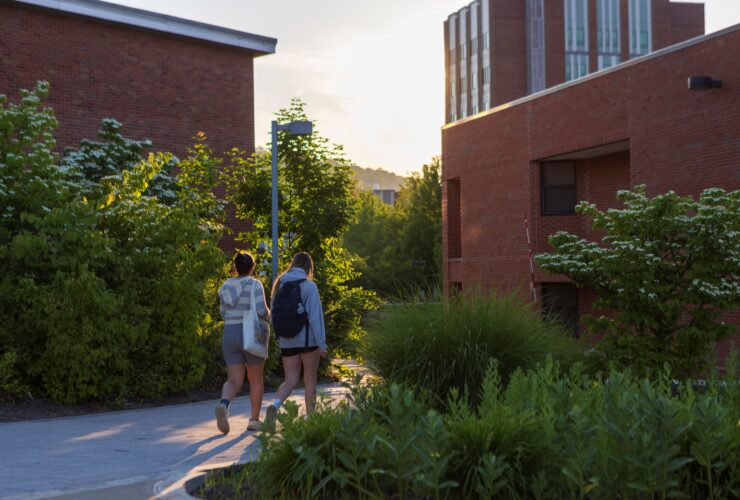 Students walk a path near Science 2 and the Science Library at sunset