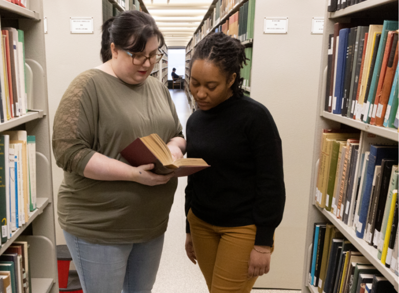 student and librarian look at a book together amongst the bookshelves in Bartle Library