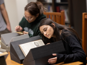 Students conduct research in the Libraries Special Collections. Photo features one student looking at a large book propped up on book supports.