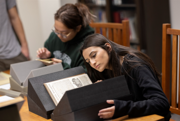 Students conduct research in the Libraries Special Collections. Photo features one student looking at a large book propped up on book supports.