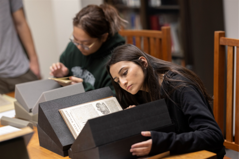 Students conduct research in the Libraries Special Collections. Photo features one student looking at a large book propped up on book supports.