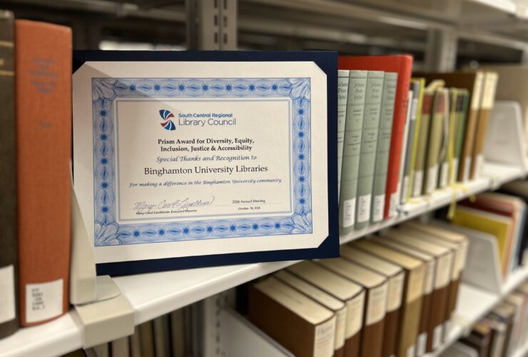 photo of the PRISM Award certificate on a bookshelf amongst various books.