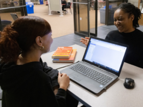 Image of a student talking to a student worker at the research help desk in Bartle Library. On the desk is an open laptop.