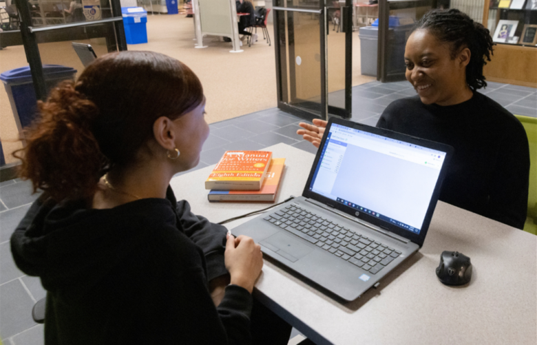 Image of a student talking to a student worker at the research help desk in Bartle Library. On the desk is an open laptop.