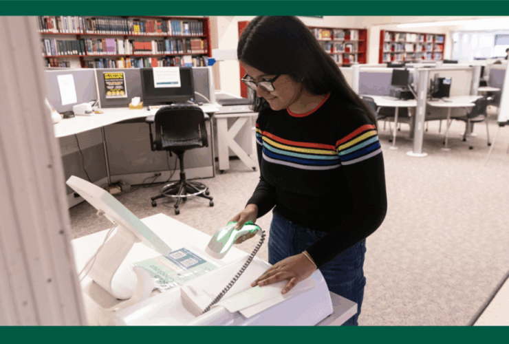 photo of student using a self-check out scanner to borrow a library book.
