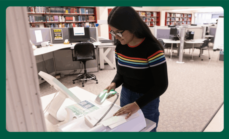 photo of student using a self-check out scanner to borrow a library book.