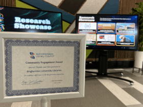 photo of Community Engagement Certificate displayed in front of the Research Showcase touchscreen displays.