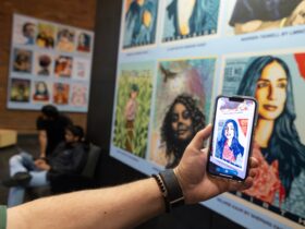 Outstretched arm holds a phone towards a collection of art portraits displayed on the first floor of Bartle Library showcasing the Augmented Reality app that animates the image.