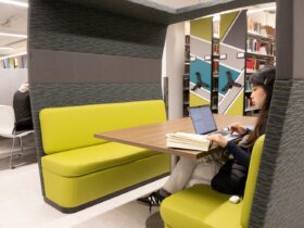 Photo of student sitting in a booth looking at a book and a laptop computer.