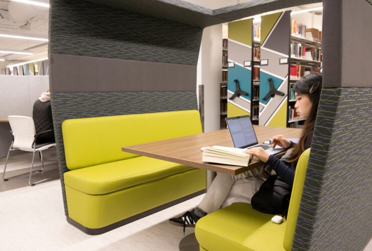 Photo of student sitting in a booth looking at a book and a laptop computer.