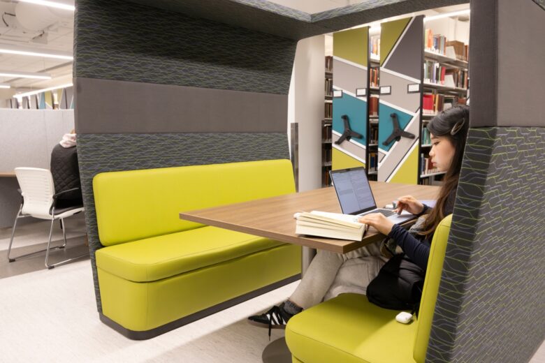 Photo of student sitting in a booth looking at a book and a laptop computer.