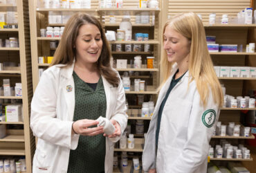 Two women from SOPPS look at a prescription bottle at Pharmacy Practice at Wegmans.