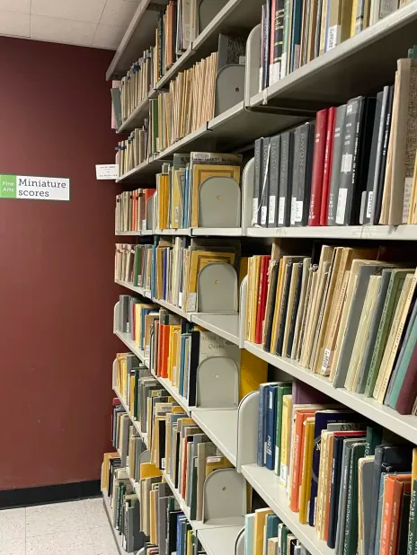 Photo of various books on a shelf labeled "Miniature scores" on the wall.