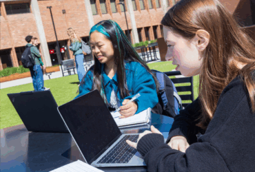 Students sitting outside Bartle Library studying on laptops.