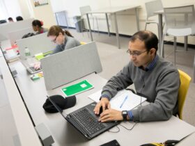 Student sits at a table working on a laptop in the Graduate Student Study Lounge.