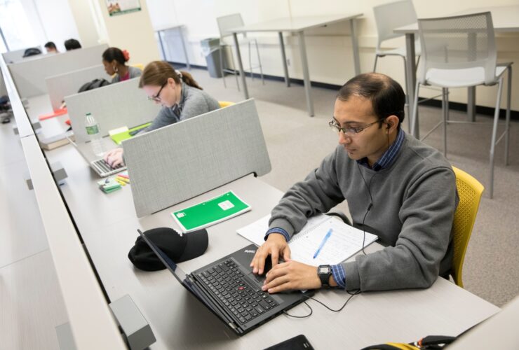 Student sits at a table working on a laptop in the Graduate Student Study Lounge.
