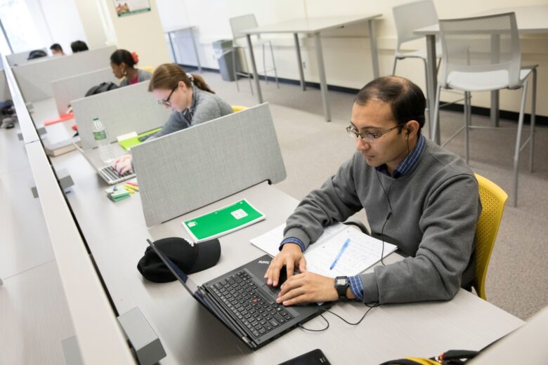 Student sits at a table working on a laptop in the Graduate Student Study Lounge.