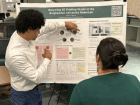 Student explains his research poster board to the Dean of Libraries by pointing at a chart.