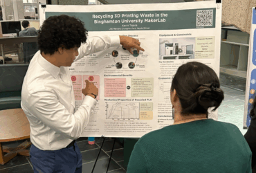 Student explains his research poster board to the Dean of Libraries by pointing at a chart.